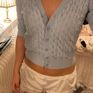 Ljusblå stickad kofta från Kappahl - Supersöt ljusblå kofta från Kappahl med v-ringning och fina stickade detaljer. Koftan har kortare ärmar, knappar framtill och ett diskret hålmönster över hela plagget. Perfekt att slänga över en topp för en fräsch look.