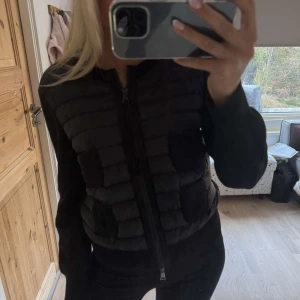 Svart cardigan jacka från Moncler - Säljer en svart cardigan jacka från Moncler med quiltad framsida och två fickor. Jackan har långa ärmar i stickat material och dragkedja framtill. Klassisk Moncler-logga på ena ärmen. Perfekt för lager-på-lager. Storleken är i M men passar mig som har storlek S vanligtvis. 