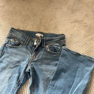 Ljusblå jeans från Gina Tricot - Säljer ett par klassiska ljusblå jeans från Gina Tricot i storlek 164. Jeansen har normal passform, raka ben och två knappar framtill. Snygga kontrastsömmar och femficksmodell. Perfekta till vardags för en avslappnad stil.