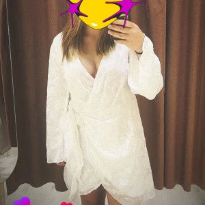 Vit omlottklänning med v-ringning - Säljer en vit omlottklänning med v-ringning och långa ärmar. Klänningen har en kort längd och en lös passform, perfekt för sommarens alla tillfällen. Enkel och stilren design som passar till många olika looks. användes på min skolavslutning i 9an så är nästintill oanvänd