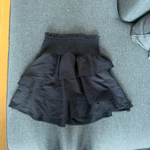 Svart volangkjol från H&M - Supersöt svart kortkjol från H&M med bred smock i midjan och flera lager volanger. Kjolen är luftig och har en snygg, flowy passform som passar perfekt till sommaren. Pris går att diskutera vid snabb affär 