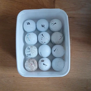 Golfbollar  - Säljer en samling med 14 vita golfbollar från bland annat Nike och Bridgestone. Bollarna ligger i en rektangulär plastlåda och har olika loggor och tryck. Perfekt för dig som vill fylla på golfbagen inför säsongen.
