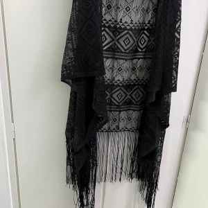 Svart kimono med fransar och mönster - Säljer en svart kimono med geometriskt mönster och långa fransar nedtill. Tunt material och öppen framtill, perfekt som lager över en topp eller klänning.