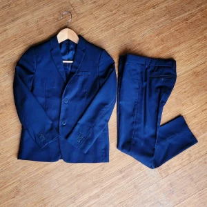 Mörkblå kostym från H&M Kille 134-140cl - Säljer en stilren mörkblå kostym från H&M i barnstorlek. Kostymen 140cl består av en kavaj med två knappar och klassiska fickor samt matchande kostymbyxor 134cl. Perfekt för speciella tillfällen som fest, begravning, nyår osv. Enbart använd 2 tillfällen så i jättefint skick!