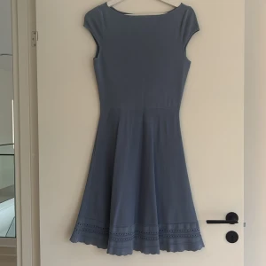 Blå klänning från H&M med håldetaljer - Säljer en ljusblå klänning från H&M med rund halsringning och korta ärmar. Klänningen har en utställd kjol med dekorativa håldetaljer och vågig kant nertill. Perfekt för vår och sommar!
