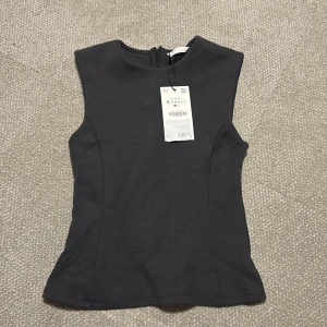 Mörkgrå topp från ZARA - mörkgrå ärmlös topp från ZARA med figurnära passform. Toppen har en diskret dragkedja i ryggen, aldrig använd prislappen kvar