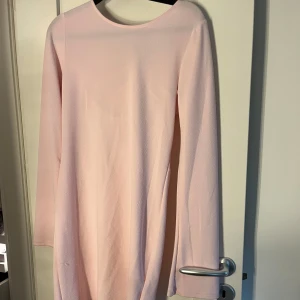 Ljusrosa långärmad klänning med öppen rygg och knyt - Säljer en ljusrosa långärmad klänning med snygg öppen rygg och knytband i nacken. Klänningen har en mjuk, något stretchig känsla och en enkel, elegant design. Perfekt för vår eller sommar.