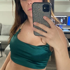 Grön oneshoulder croppad topp - Säljer en smaragdgrön  topp med croppad passform. Toppen har en bred axelrem i kedjedesign i guld och är tillverkad i ett glansigt, slätt material. 💚