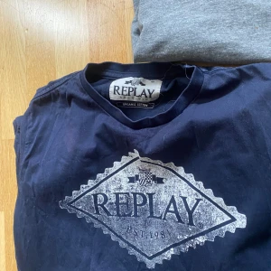 Mörkblå t-shirt från Replay - Säljer en mörkblå t-shirt från Replay med stort vitt tryck på bröstet. T-shirten är i bomull och har en klassisk rund hals. Perfekt för dig som gillar stilrena logotyper och bekväma plagg.