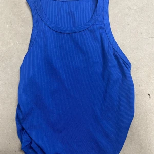 Blå ribbad linnetopp - Säljer en blå ribbad linnetopp i storlek S. Toppen har en klassisk ärmlös design med rund halsringning och är tillverkad i ett stretchigt material som sitter skönt mot kroppen. Perfekt för varma dagar eller som lager under en skjorta.
