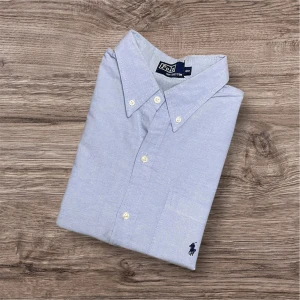 Ralph Lauren Kortärmad Skjorta  - Ralph Lauren Kortärmad Skjorta – Ljusblå (L)💙👔  Säljer en snygg och luftig kortärmad skjorta från Ralph Lauren i ljusblå färg. Perfekt till sommaren – enkel att styla både uppklätt och avslappnat! Billigt pris på grund av defekt – se sista bilderna.  ✅ Storlek: L 📏 Mått: Längd 70 cm, armhåla till armhåla 60 cm, axel till axel 50 cm 🎨 Färg: Ljusblå 👕 Modell: Kortärmad skjorta 🏷 Märke: Ralph Lauren 🛍 Nypris ca 1800 kr  📍 Finns i Linköping – kan skickas mot fraktkostnad. 94 