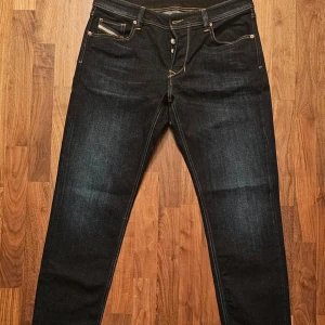 Diesel jeans - Straight fit - W34 L32  - Snygga mörkblå jeans från Diesel med klassisk femficksdesign och kontrastsömmar. Perfekta för en stilren look. Märkesdetaljer på fickan och etikett bak. Passar bra till både sneakers och kängor.