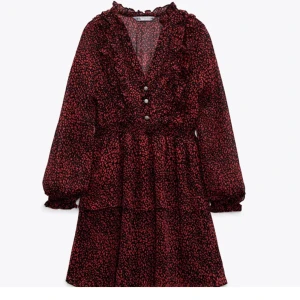 Svart och röd mönstrad klänning från Zara - Supersöt klänning från Zara i svart och rött med småprickigt mönster. Klänningen har volangdetaljer, v-ringning, knappar framtill och långa ärmar med resår vid handlederna. Perfekt för dig som gillar romantisk stil!