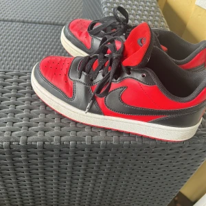 Nike Air Jordans svart och röda sneakers - Säljer ett par klassiska Nike Air Jordans i svart och rött med vit sula. Skorna har snörning och den ikoniska swoosh-loggan på sidan. Perfekta för dig som gillar streetwear och vill sticka ut med snygga färger.