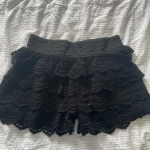 Volang shorts spets shorts  - Svarta shorts med bred resår i midjan och flera lager volang i virkad spets. De har en feminin och bohemisk stil med fina detaljer och vågig kant nertill. Perfekta för sommardagar eller festival. Aldrig använt!