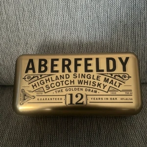 Aberfeldy Highland Single Malt Scotch Whisky presentask  - Säljer en snygg presentask i metall från Aberfeldy Highland Single Malt Scotch Whisky, 12 Years in Oak. Asken är guldig med svart text och har plats för en flaska whisky. Perfekt som samlarobjekt eller för att ge bort en exklusiv present. (ÄR BARA LÅDAN)