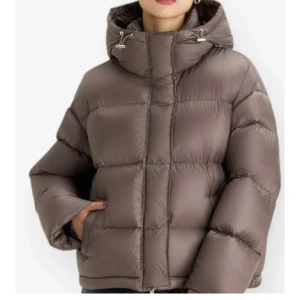 Brun pufferjacka med huva - Säljer en snygg brun pufferjacka med huva. Jackan är perfekt för kalla dagar och har en dragkedja framtill. Den är i ett puffigt material som håller dig varm och mysig. Passar perfekt för höst och vinter. Prislapp kvar