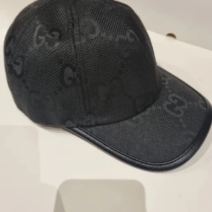 Svart keps från Gucci med GG-mönster - Snygg svart keps från Gucci med diskret GG-logga i mönstret. Kepsen har böjd skärm och justerbar rem baktill. Materialet är strukturerat och ger en exklusiv känsla.