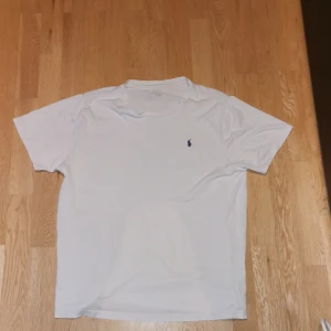 Vit t-shirt från Ralph Lauren - Tjena! Jag säljer en vit klassisk t-shirt från Ralph Lauren med liten broderad logga i mörkblått på bröstet. T-shirten har rund hals och korta ärmar, perfekt för en clean och enkel stil. Halsen är ganska utöjd och tröjan är i okej skick därav det låga priset.