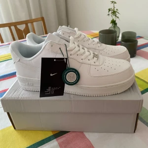 Nike Air Force 1  - Säljer ett par klassiska vita Nike Air Force 1 '07 sneakers. Skorna har en stilren design med perforerad tå, snörning och platt sula. Perfekta för dig som gillar tidlös streetstil och vill ha ett par fräscha sneakers i garderoben. Splitternya från Stock  X köpta för 1799. Skriv vid minsta lilla fundering. Ej äkta 