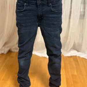 Mörkblå jeansbyxor - Säljer ett par mörkblå jeansbyxor  med klassisk femficksdesign och raka ben. Jeansen har normal passform och är tillverkade i ett slitstarkt denimtyg. Perfekta för dig som gillar en tidlös stil.