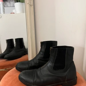 Svarta ridstövletter från CRW med dragkedja - Säljer ett par svarta ridstövletter från CRW med dragkedja framtill. Mest slitna i färgen där framme annars i bra skick! Storlek 39