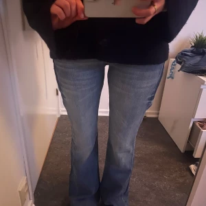 Blå bootcut jeans från Cross - Snygga blå bootcut jeans från Cross med klassisk femficksdesign och broderade bakfickor. Perfekta för en avslappnad stil med en touch av retro. De har en knappgylf och är tillverkade i slitstarkt denim.