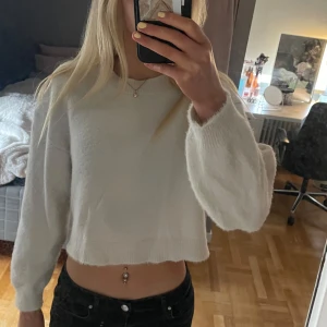 Vit croppad stickad tröja - Säljer en vit croppad stickad tröja med lång ärm. Tröjan har en avslappnad passform och är perfekt för lager-på-lager. Enkel och stilren design som passar till mycket.