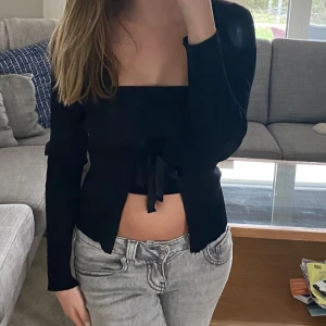 Svart ribbad croppad kofta från Massimo Dutti - Svart ribbad kofta från Massimo Dutti i croppad modell med knyt framtill. Långärmad och i mjukt, stretchigt material som sitter snyggt på kroppen. Perfekt att styla med jeans eller kjol för en trendig look.