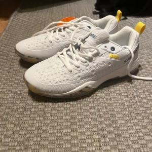 Vita sneakers från Salming - Snygga vita sneakers från Salming med ett unikt hexagonmönster på ovansidan. Skorna har snörning och gula detaljer vid hälen. Perfekta för både träning och vardag.