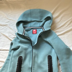 Ljusblå huvtröja från Nike - Säljer en ljusblå huvtröja från Nike med dragkedja och svarta detaljer. Tröjan har en bekväm passform och är perfekt för vardagliga aktiviteter. Den har långa ärmar och en praktisk huva. Smutsig Ska Tvätta Den