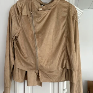 Beige jacka från Flash Woman - Snygg beige mocka jacka från Flash Woman med dragkedja och stilren design. Jackan har långa ärmar och en modern look som passar perfekt för höst och vår. Perfekt för dig som vill ha en stilren och bekväm jacka. Helt ny! 