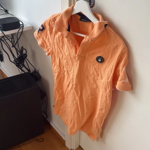 Orange pikétröja från Parajumpers - Säljer en snygg orange pikétröja från Parajumpers. Tröjan har korta ärmar och en klassisk krage med knappar. Perfekt för en avslappnad stil.