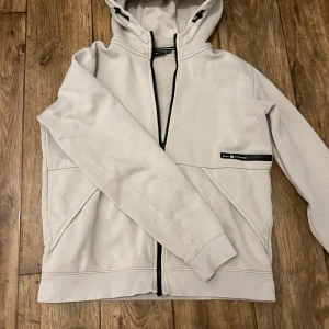 Beige huvtröja från Sail Racing - Säljer en stilren beige huvtröja från Sail Racing. Tröjan har en dragkedja framtill och en justerbar huva. Kan tänka mig sänka priset vid snabb affär. Bara att skriva om ni undrar något!