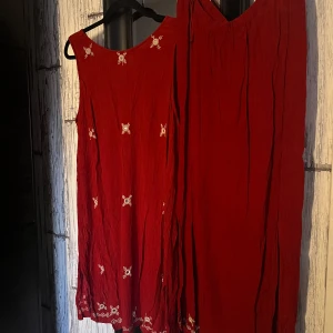 Röd ärmlös klänning med broderi - Säljer en röd ärmlös klänning med vackra broderade detaljer. Klänningen har en lös passform och är perfekt för varma dagar. Den har en fin struktur i tyget som ger en extra dimension till looken.