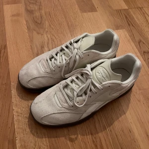 Vita sneakers från Reebok - Snygga vita sneakers från Reebok i mocka med klassisk design. Skorna har snörning och en bekväm passform, perfekt för vardagsbruk. Den neutrala färgen gör dem lätta att matcha med olika outfits.