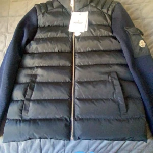 Svart dunväst från Moncler - Snygg svart dunväst från Moncler med dragkedja och quiltad design. Perfekt för kyligare dagar med sin vattenavvisande och vindtäta funktion. Västen har praktiska innerfickor och en stilren look.