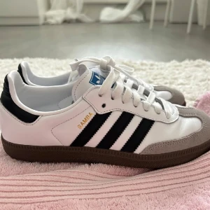 Adidas Samba i vitt och svart - Klassiska Adidas Samba sneakers i vitt med svarta ränder och brun sula. Nyskick storlek 37,5