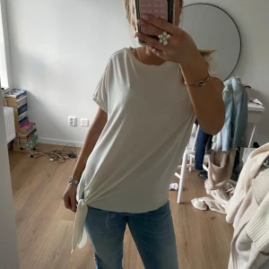 Vit t-shirt med knyt - Säljer en stilren vit t-shirt med korta ärmar och en snygg knytning på sidan. Perfekt för en avslappnad look.