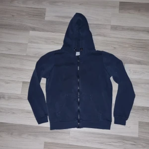 Mörkblå hoodie från Stories - Säljer en stilren mörkblå hoodie från Stories i storlek S. Tröjan har en dragkedja framtill och en praktisk huva. Perfekt för en avslappnad look.