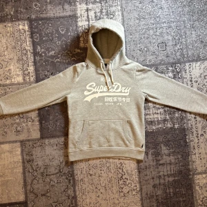 Grå superdry hoodie  - Säljer en fin superdry hoodie som är i färgen grå och storlek M/S. tröjan är i otroligt bra skick. skulle säga att tröjan passar bra i s men litet i m. Så om du är mellan dessa storlekar så är de här tröjan perfekt för dig. Har du några andra frågor är det bara att hojta till !