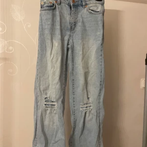 Ljusa jeans med slitningar - Säljer ett par ljusa jeans med coola slitningar på knäna. De har en klassisk femficksdesign och knappgylf. Perfekta för en avslappnad stil.