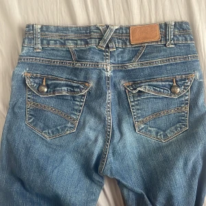 Blå jeans med dubbla knappar - Snygga blå jeans med dubbla knappar och dekorativa bakfickor. De har en klassisk femficksdesign och bälteshällor. Innerbenslängd: 72 cm och midjemått: 36 cm.❤️