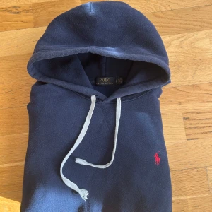 Mörkblå hoodie från Polo Ralph Lauren - Säljer en snygg mörkblå hoodie från Polo Ralph Lauren med en röd logga på bröstet. Den har en justerbar huva med vita snören.