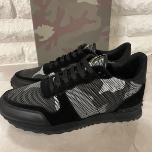 Valentino rockrunners  - Snygga Valentino sneakers med ett coolt kamouflagemönster i svart och grått. Skorna har snörning och en unik design med detaljer i mocka och syntetmaterial. Perfekta för att ge din outfit en edgy touch. Dom är lite stora i storleken 