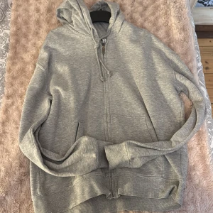 Grå hoodie med dragkedja - Säljer en bekväm grå hoodie med dragkedja och huva. Perfekt för en avslappnad stil. Den har långa ärmar och ribbade muddar vid ärmslut och nederkant. Från HM i storlek xs