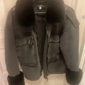 Svart jacka med pälsdetaljer från boohoo - Snygg svart jacka från Boohoo med mjuka pälsdetaljer på krage och ärmslut. Jackan har en dragkedja framtill och stora fickor på bröstet. Perfekt för att hålla sig varm och stilren under kyliga dagar.