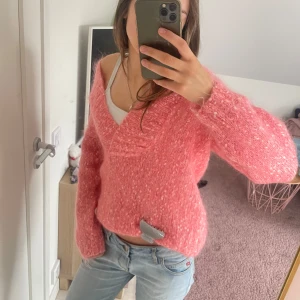 Rosa stickad tröja - Säljer en mysig rosa stickad tröja med en v-ringad design. Tröjan har en croppad passform och långa ärmar, perfekt för en avslappnad stil. Den är både trendig och bekväm, idealisk för kyligare dagar. Egen stickad men köpt på Vinted