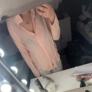 Ljusrosa blus med knappar - Säljer en ljusrosa blus med långa ärmar och knappar framtill. Blusen har en klassisk krage och är tillverkad i ett tunt, lätt material som ger ett luftigt intryck. Perfekt för dig som gillar en feminin och stilren look.