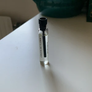 Jardin de Flora Essnce parfymtester - Liten parfymprovflaska från Jardin de Flora med texten 'ESSENCE' på etiketten. Flaskan är genomskinlig med svart plastlock och innehåller en klar vätska. Perfekt för att testa doften innan köp av större flaska.